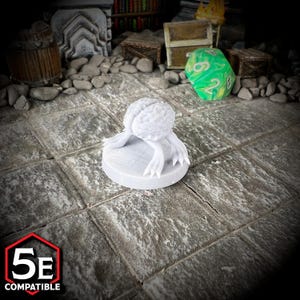 May include: A white, 3D-printed miniature of a brain with tentacles, designed for tabletop gaming. The miniature is on a round base and is labeled "5E COMPATIBLE" in a red and white hexagon.