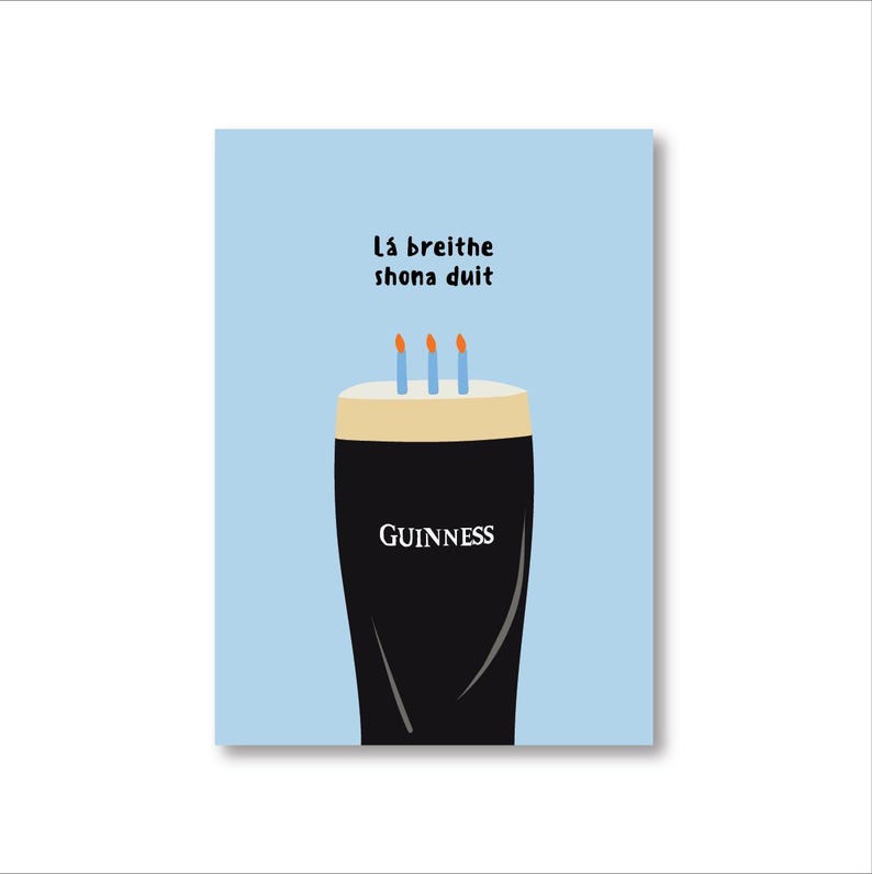 May include: A greeting card with a light blue background features a stylized illustration of a pint of Guinness with three lit candles on top. The word "GUINNESS" is printed on the glass. The text "L&aacute; breithe shona duit" is printed above the pint.
