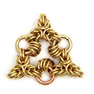 Puede incluir: Un colgante de cadena de metal de color dorado en forma de tri&aacute;ngulo. El colgante est&aacute; hecho de m&uacute;ltiples anillos entrelazados.