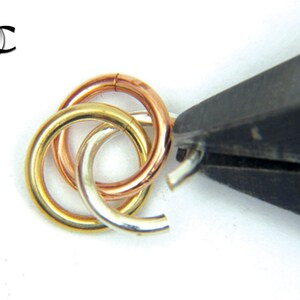 Puede incluir: Primer plano de tres anillos entrelazados, uno de oro, uno de plata y uno de oro rosa, que se cierran con unas pinzas.