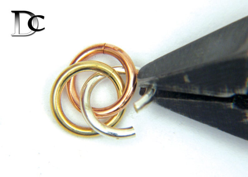 Puede incluir: Primer plano de tres anillos entrelazados, uno de oro, uno de plata y uno de oro rosa, que se cierran con unas pinzas.