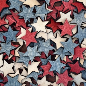 May include: A collection of wooden stars in red, white, and blue. The stars are scattered on a dark brown surface.