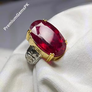 Op de afbeelding: Een gouden ring met een grote, ovale robijn. De ring heeft een gedetailleerd bloemmotief op de band.