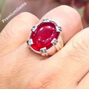 May include: A silver ring with a large, oval, deep red gemstone. The gemstone is set in a silver band with decorative accents. The text "PremiumGems" is visible in the upper left corner.