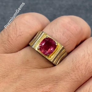 Könnte beinhalten: Ein Goldring mit einem zentralen, kissenförmigen, tiefrosa Edelstein in einer Vier-Krappen-Fassung. Die Ringschiene hat ein breites, strukturiertes Design mit vertikalen Rillen auf beiden Seiten des Steins. Der Text PremiumGems ist zu sehen.