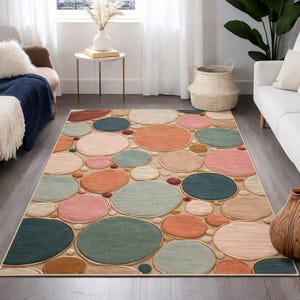 May include: A rectangular area rug featuring a pattern of colorful, overlapping circles in shades of pink, orange, teal, and green. The circles are set against a neutral beige background, creating a modern and playful design for home decor.