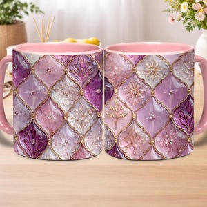 May include: Two ceramic mugs with a pink interior and handle. The exterior features a mosaic design in shades of purple, white, and gold. The mosaic pattern includes floral and geometric shapes. The mugs are placed on a wooden surface.