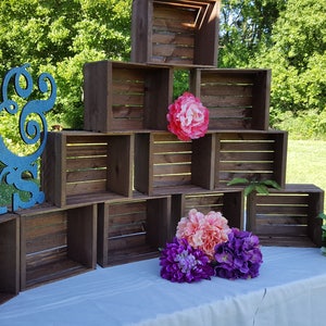 May include: A wooden crate display with a blue glitter "Mr & Mrs" sign. The display is decorated with colourful flowers, including pink, purple, and green, and is set on a white tablecloth.