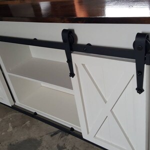 May include: White cabinet with two sliding barn doors. The doors have a white X pattern and black hardware. The cabinet has a dark brown top and two shelves inside.