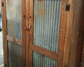 May include: A rustic wooden cabinet with two doors. The doors are made of corrugated metal with a rusty patina. The cabinet has a dark brown stain and is accented with black metal hinges.