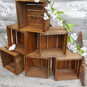 May include: A set of six wooden crates stacked in a pyramid shape. The crates are made of natural wood and have a rustic, distressed look. The crates are empty and ready to be used for storage or display.
