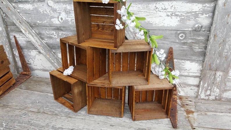 May include: A set of six wooden crates stacked in a pyramid shape. The crates are made of natural wood and have a rustic, distressed look. The crates are empty and ready to be used for storage or display.