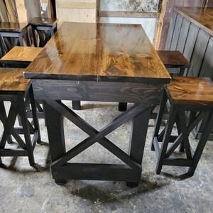 May include: A set of four black wooden bar stools with a brown wood top and a criss-cross design on the legs. The stools are arranged around a black wooden table with a brown wood top.