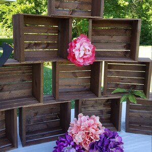 May include: A tiered display of dark brown wooden crates, with pink and purple floral arrangements. The crates are arranged to create a display. The flowers provide a vibrant contrast to the wooden crates.