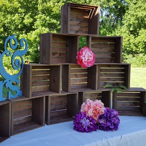 May include: A display of stacked wooden crates, forming a tiered structure. A large teal glitter sign reading "Mr & Mrs" is on the left. The display is decorated with colourful artificial flowers, including pink, purple, and green.