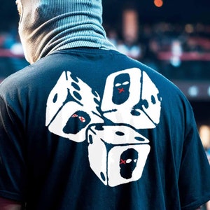 Peut inclure: Un t-shirt noir avec un motif blanc de trois dés avec des visages masqués. Les dés sont empilés les uns sur les autres.