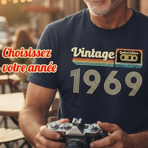 Peut inclure: T-shirt bleu marine avec l'inscription "Vintage 1969" et un graphisme de cassette rétro. Le t-shirt porte également l'inscription "Limited Edition". La personne tient un appareil photo vintage.