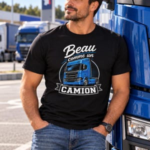 May include: A black short-sleeved t-shirt featuring a graphic print of a blue semi-truck inside a circular frame. The text "Beau comme un CAMION" is printed in white and blue above and below the truck illustration on the front of the shirt.