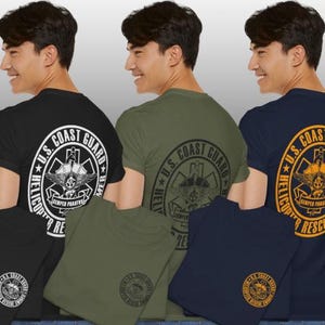 May include: Three t-shirts in black, olive green, and navy blue, each featuring a U.S. Coast Guard design on the back. The design includes text and a circular emblem with a helicopter and the words "Helicopter Rescue Swimmer".