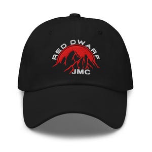 Puede incluir: Gorra de béisbol negra con visera curva. La gorra presenta un diseño bordado de una cordillera roja y las palabras "RED DWARF" en blanco, arqueadas sobre las montañas. Las iniciales "JMC" están bordadas debajo.
