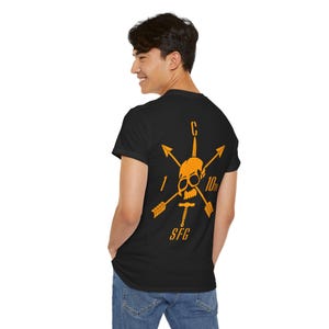 Könnte beinhalten: Schwarzes T-Shirt mit einem orangefarbenen Aufdruck auf der Rückseite, der einen Totenkopf, Pfeile und den Text "10th SFG" zeigt. Das Design ist zentriert und auffällig. Das T-Shirt hat einen klassischen Rundhalsausschnitt.