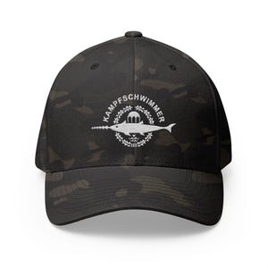 May include: Black camouflage baseball cap with a white circular emblem featuring a narwhal and the text "KAMPFSCHWIMMER". The cap has a curved peak and a structured fit, suitable for outdoor activities.