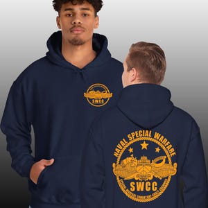 May include: Navy blue hoodie with a gold embroidered logo on the front and back. The logo features a submarine and the text "NAVAL SPECIAL WARFARE SWCC SPECIAL WARFARE COMBATANT-CRAFT CREWMAN".