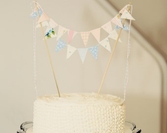 Adorno para tarta con banderines rosas y azules, con un toque de carnaval vintage. Ideal para baby showers, cumpleaños y celebraciones informales con un toque rústico.