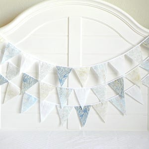 May include: A white string of bunting with blue and white patterned fabric triangles. The bunting is hanging on a white headboard.