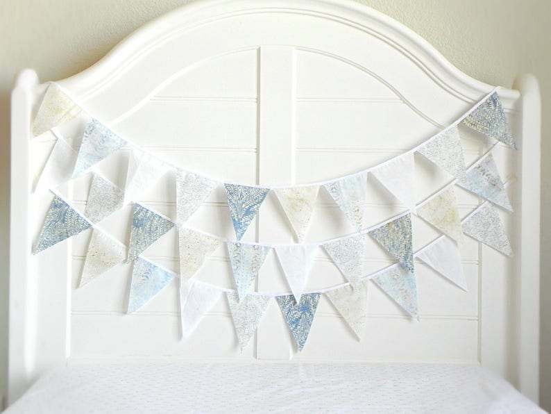 May include: A white string of bunting with blue and white patterned fabric triangles. The bunting is hanging on a white headboard.