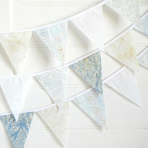 May include: A white and blue patterned bunting with triangular flags. The flags have a white border and are strung together with white string.
