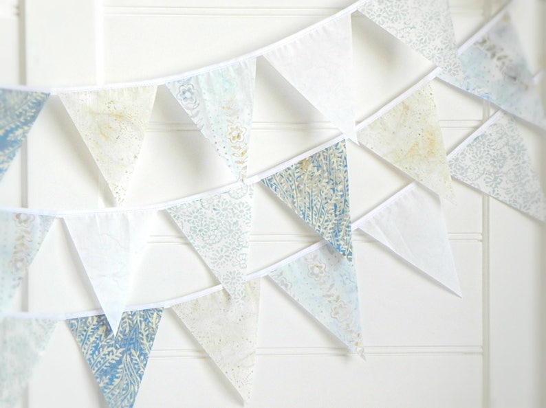 May include: A white and blue patterned bunting with triangular flags. The flags have a white border and are strung together with white string.