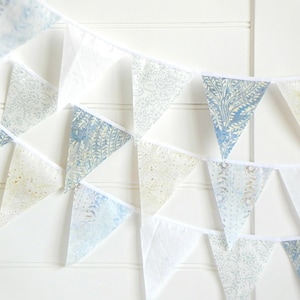 May include: A blue and white patterned bunting with triangular flags. The flags are made of a light fabric and have a white trim. The bunting is strung on a white cord.