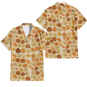 May include: A short-sleeved shirt with a repeating pattern of cartoon buttocks in shades of brown, tan, and orange on a cream background. The shirt has a classic collar and a relaxed fit, with a second shirt visible in the background.