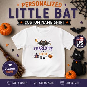 May include: A white short-sleeved t-shirt featuring a graphic of a bat, a haunted house, and a jack-o'-lantern. The text reads "CHARLOTTE LITTLE BAT". The design includes stars and a crescent moon. The shirt is surrounded by Halloween-themed decorations.