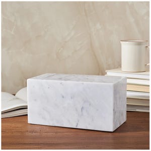 May include: A white marble rectangular bookend with a veined pattern. The bookend is sitting on a wooden surface.