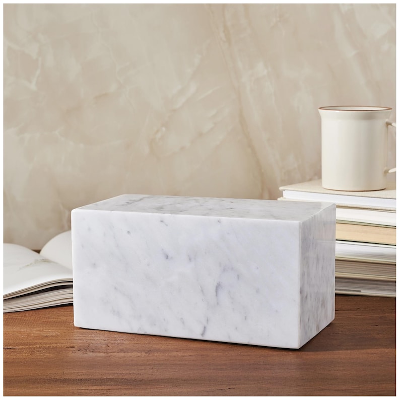 May include: A white marble rectangular bookend with a veined pattern. The bookend is sitting on a wooden surface.