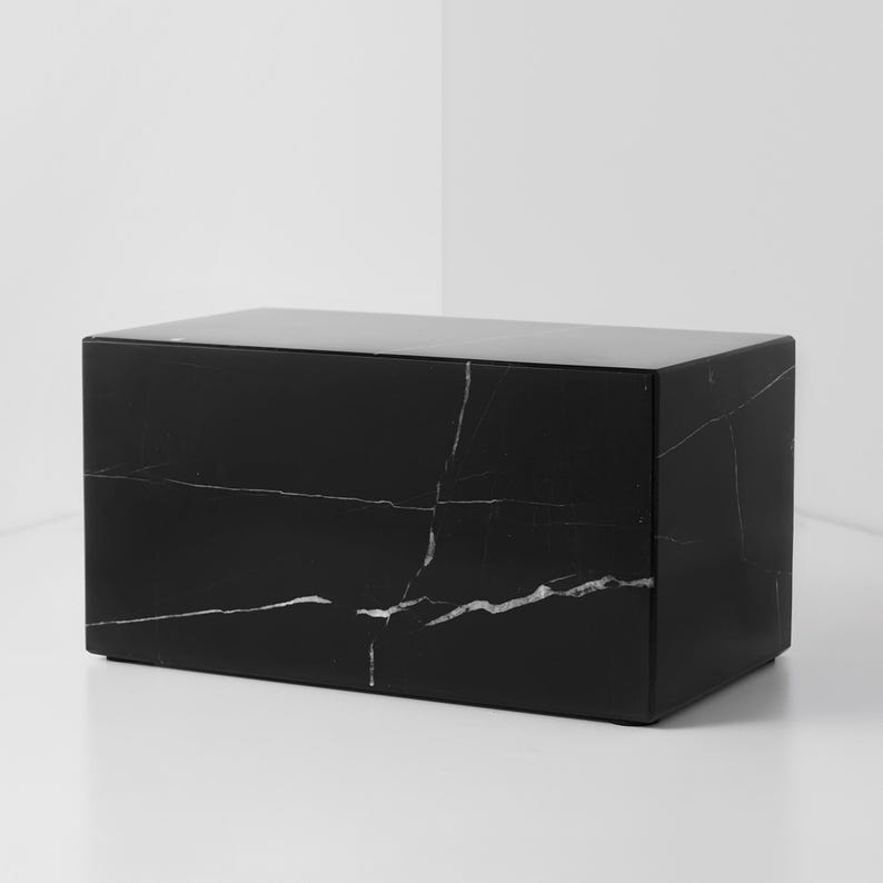 May include: A rectangular black marble box with white veining. The box has a smooth, polished surface and a minimalist design. The marble has a natural pattern, adding visual interest to the piece. This decorative box is suitable for home decor.