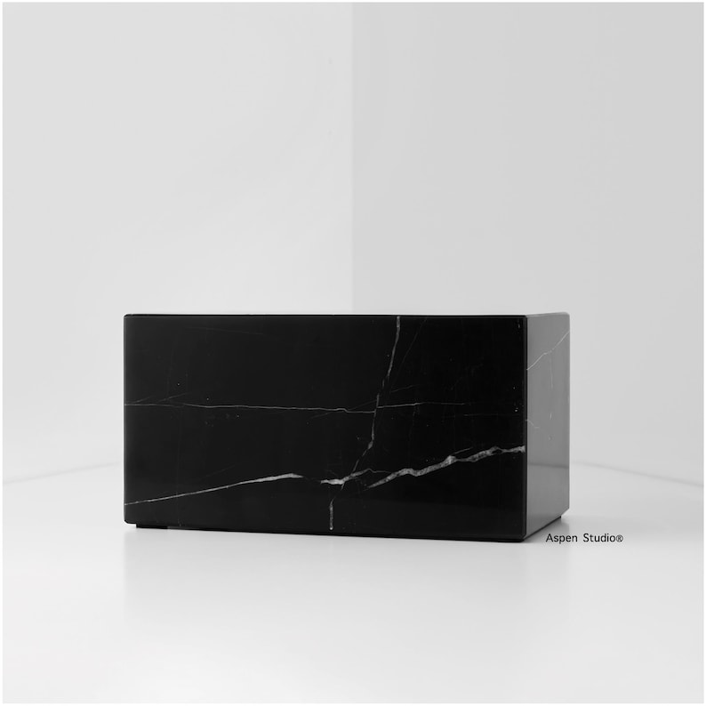 May include: A rectangular black marble block with white veining. The polished stone has a smooth surface and is set against a white background. The block is a solid, geometric shape, suitable for display or as a decorative element.