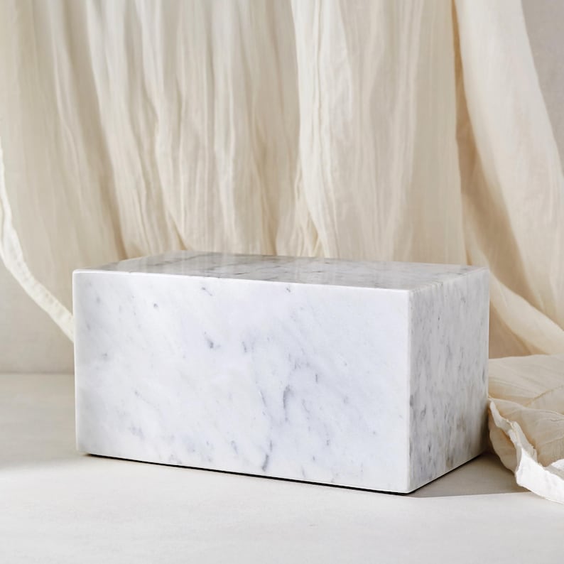 May include: White marble rectangular block with a smooth surface and subtle gray veining. The block is sitting on a white surface.