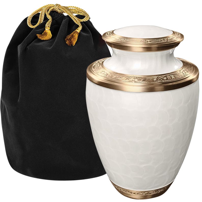 May include: A white urn with a textured pattern, accented with gold-colored bands and a matching lid. A black velvet bag with a gold drawstring is next to the urn. The urn is designed for memorial purposes.