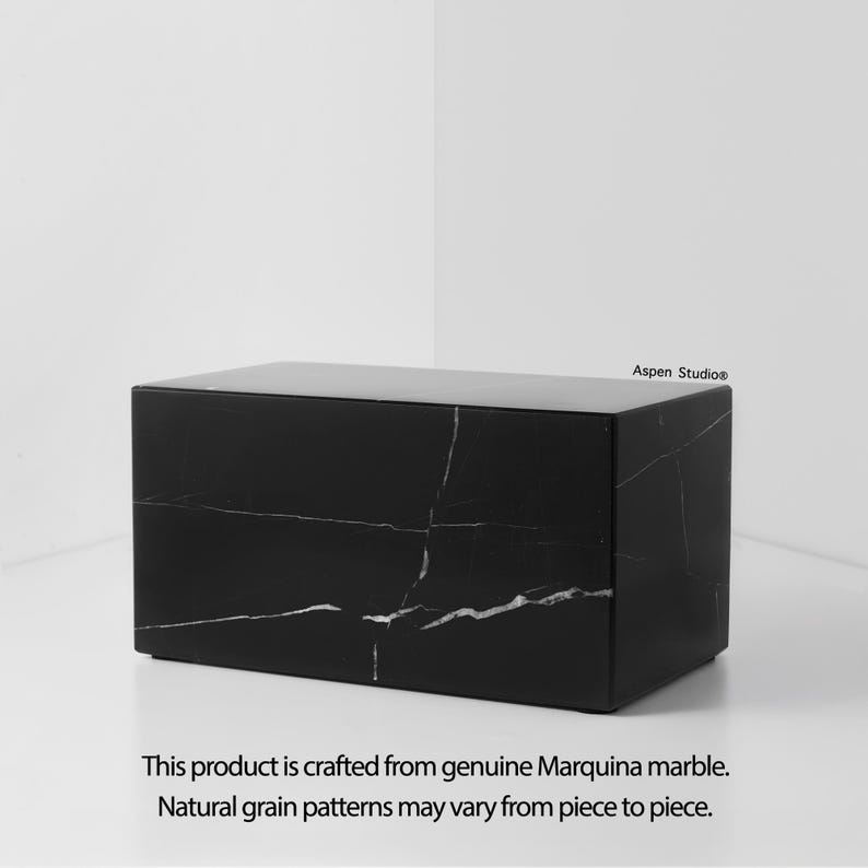 May include: A rectangular black marble box with white veining. The product is crafted from genuine Marquina marble. The text "Aspen Studio&reg;" is in the upper right corner. The text "This product is crafted from genuine Marquina marble. Natural grain patterns may vary from piece to piece." is at the bottom.