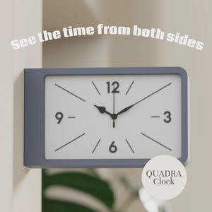 May include: A rectangular wall-mounted clock with a gray frame and a white face featuring black numerals at 3, 6, 9, and 12 o'clock. The text "See the time from both sides" appears above the clock, and a circular label reads "QUADRA Clock".