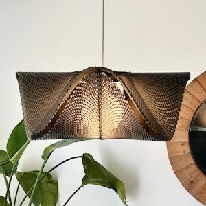 May include: A pendant light fixture featuring a dark brown, textured, geometric shade with a repeating grid pattern. The shade has a wide, angular, open-ended design that tapers toward the center, where a single warm light bulb is visible.