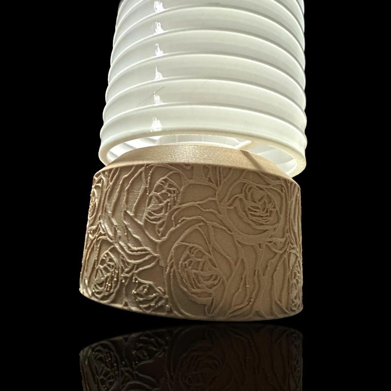 May include: A white lampshade with a brown base featuring a rose pattern. The lampshade is made of a ribbed material and has a cylindrical shape.