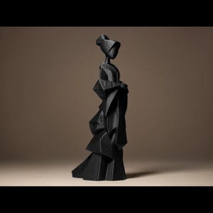 Può includere: Scultura nera di una donna con un lungo abito e cappello. La figura ha una silhouette snella e l'abito ha un design a strati, simile all'origami. La scultura è ambientata su uno sfondo neutro.