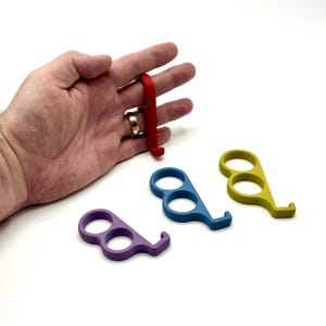 Könnte beinhalten: Eine Sammlung farbenfroher Türöffner-Werkzeuge aus Kunststoff in Rot, Blau, Gelb und Lila. Die Werkzeuge haben eine Fingerschlaufe und einen Haken zum Öffnen von Türen und Drücken von Knöpfen.