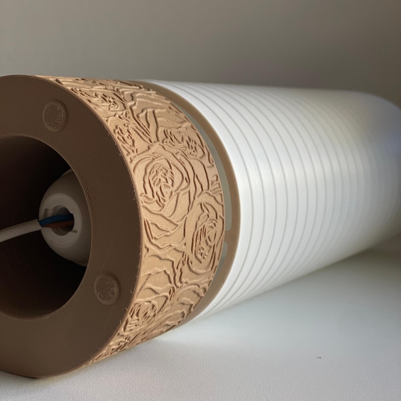 May include: A brown cylindrical lampshade with a floral pattern and a white striped base. The lampshade has a hole at the top for a light bulb.