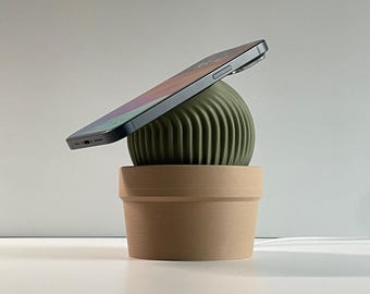 May include: A green cactus-shaped wireless charging stand with a brown ceramic pot. A black smartphone is charging on the stand.