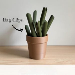 Könnte beinhalten: Ein Terrakotta-Topf gefüllt mit grünen Beutelclips. Der Text "Bag Clips" steht über dem Topf.
